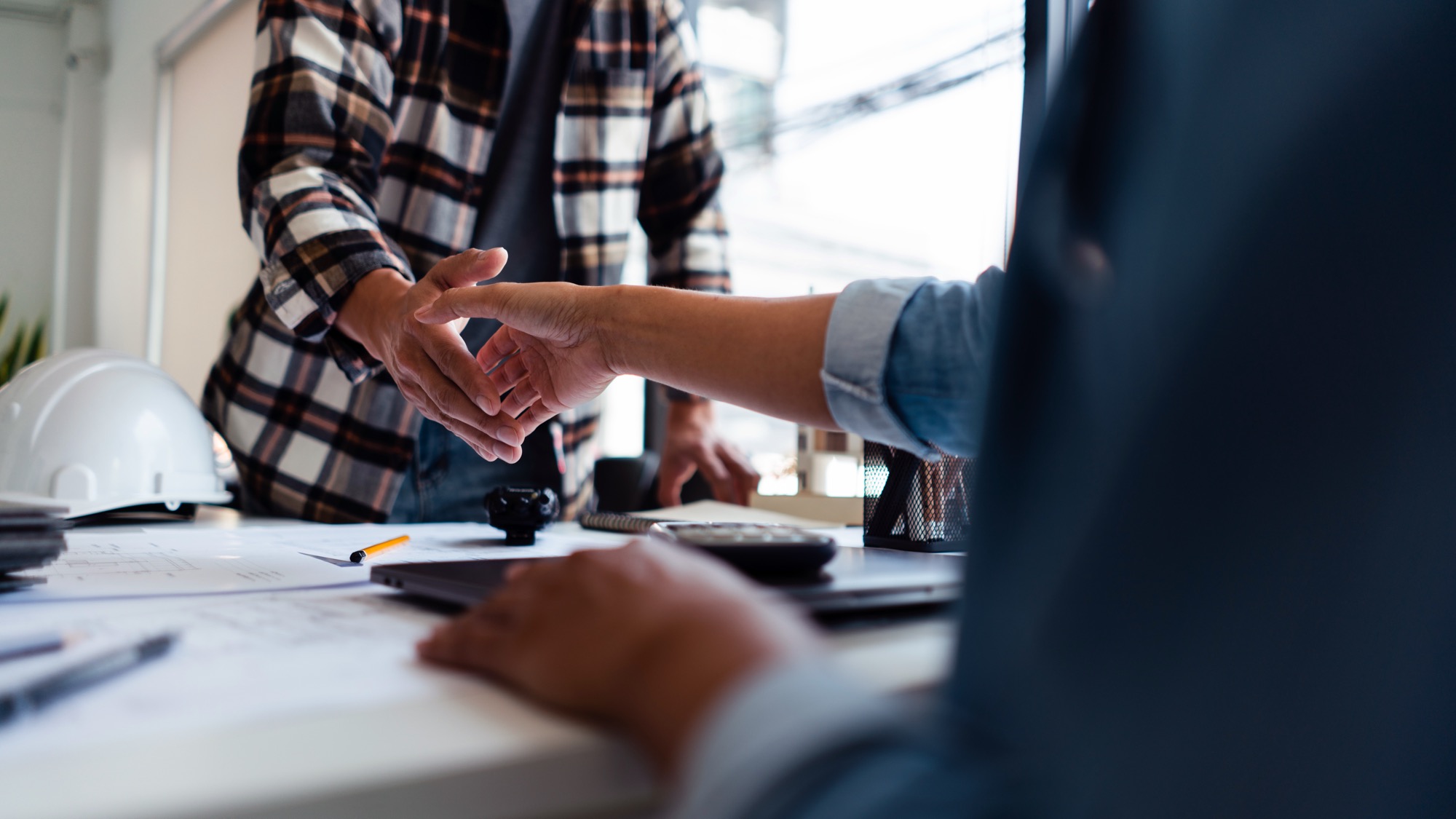 Two people shaking hands across a desk of project documents