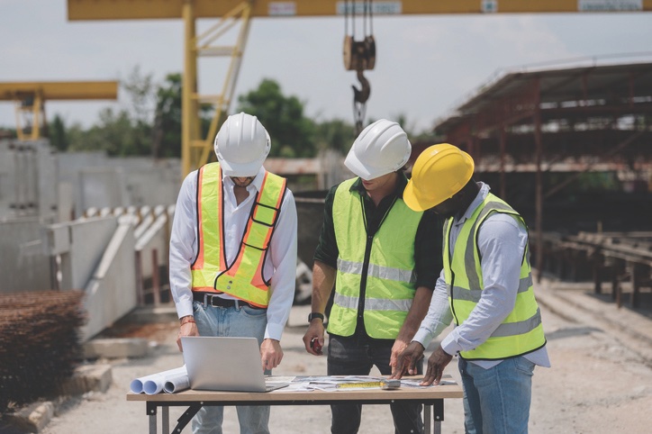 Three site managers in hard hats and safety vests reviewing drawings on a job site